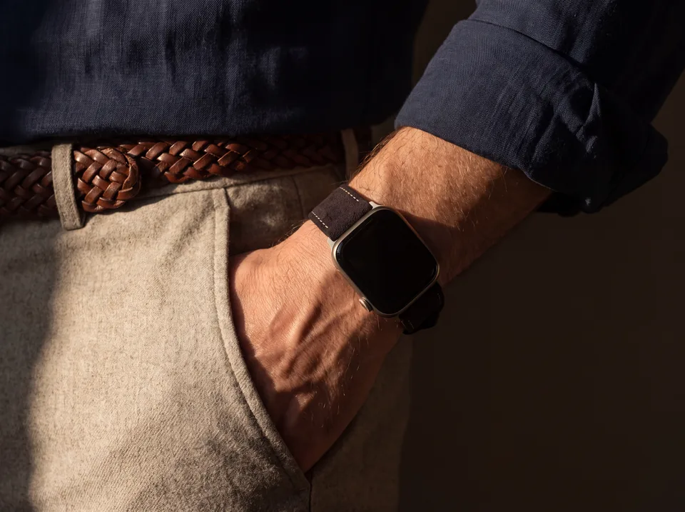 Mann in Leinenhemd und beiger Hose mit geflochtenem Gürtel trägt eine Apple Watch mit dunkelbraunem Alcantara-Armband von INDISTRAPS