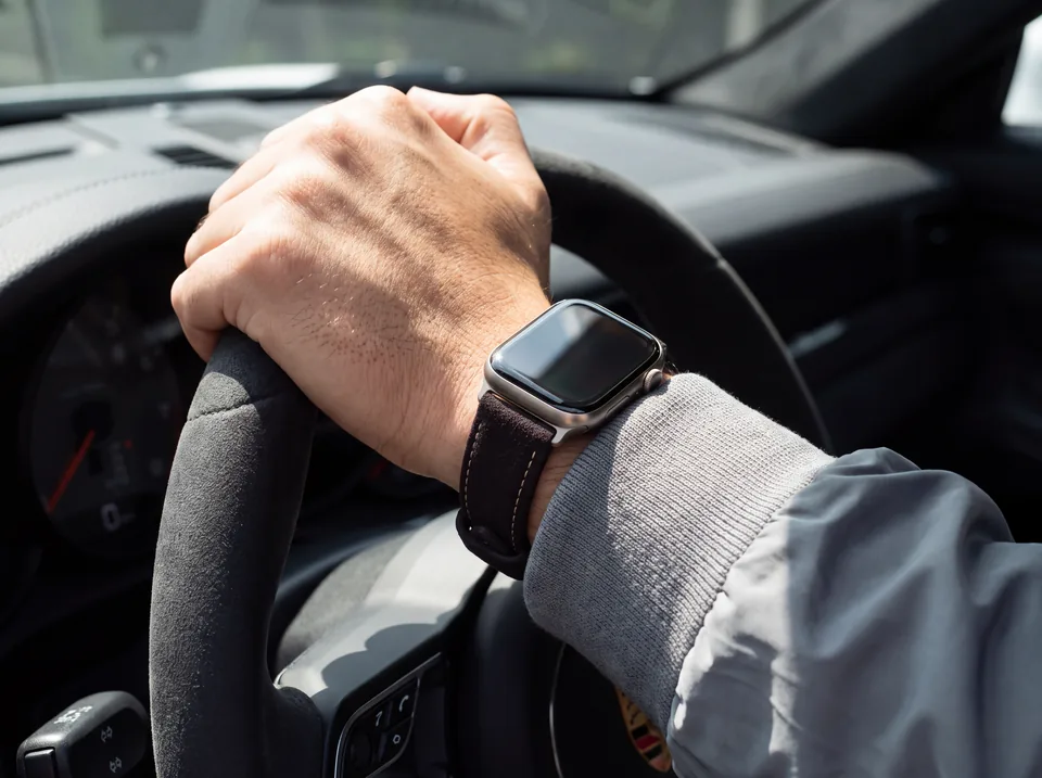 Hand am Alcantara-Lenkrad eines Sportwagens, Apple Watch mit dunkelbraunem Alcantara-Armband von INDISTRAPS