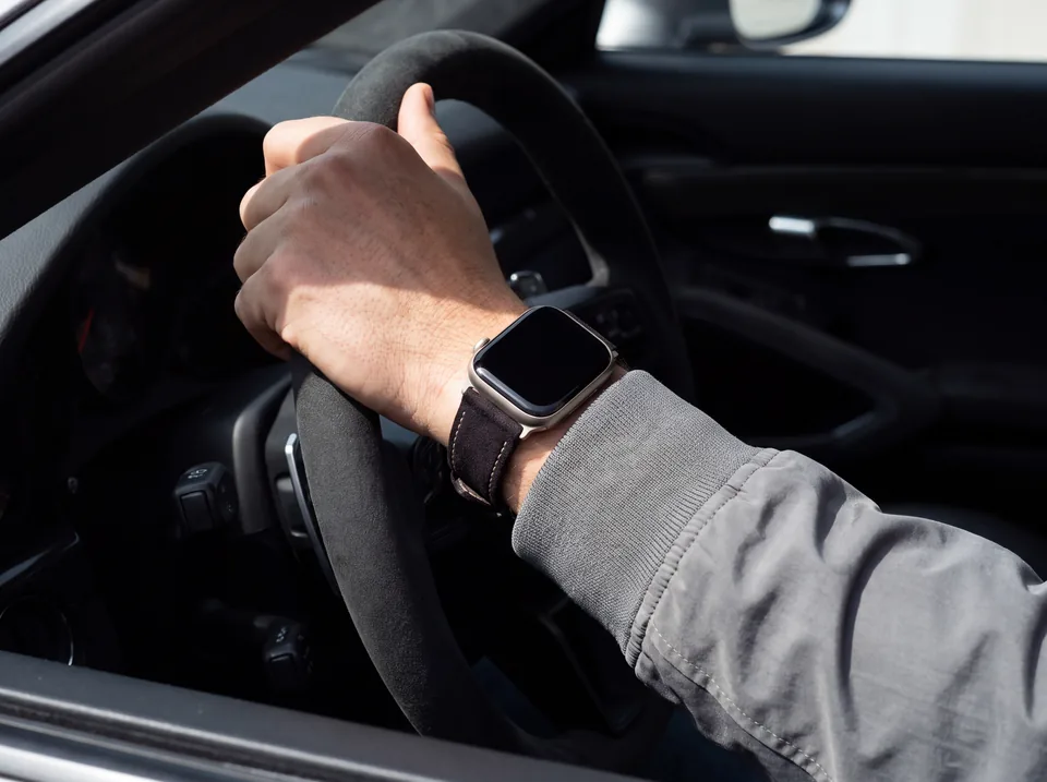 Apple Watch mit dunkelbraunem Alcantara-Armband von INDISTRAPS am Lenkrad eines Sportwagens – Variante