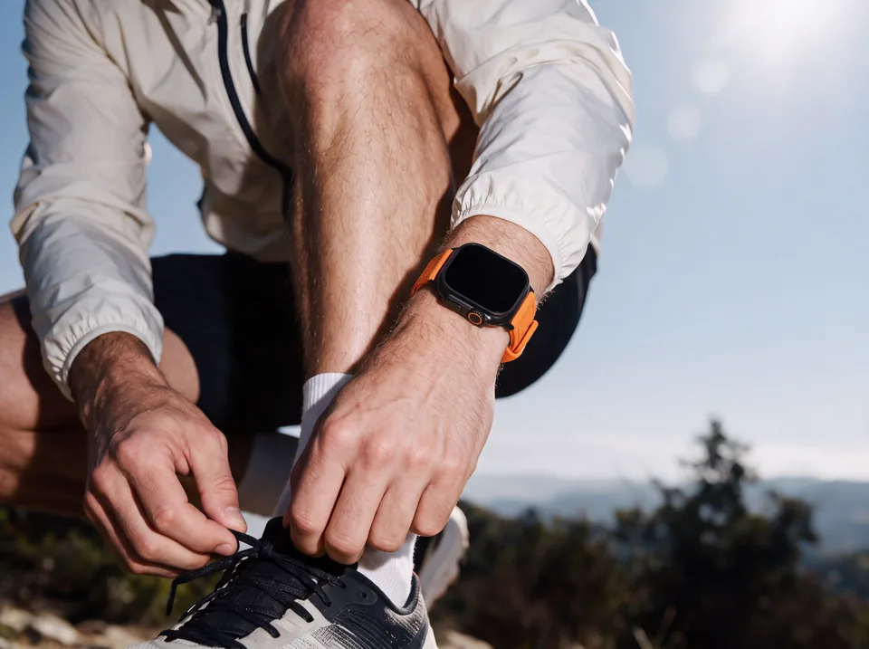Trailrunner bindet in den Bergen seine Laufschuhe und trägt eine Apple Watch mit orangefarbenem Canvas-Armband von INDISTRAPS