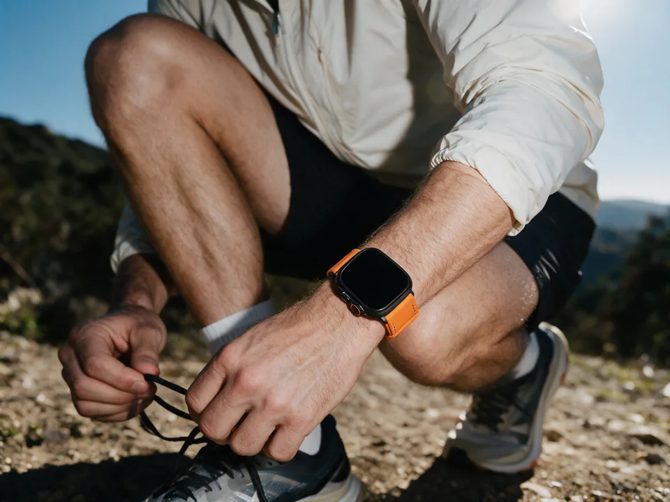 Trailrunner bindet in den Bergen seine Laufschuhe und trägt eine Apple Watch mit orangefarbenem Canvas-Armband von INDISTRAPS