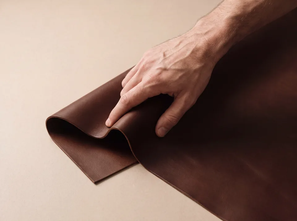 Hand streicht über eine gefaltete dunkelbraune Lederhaut auf einem hellen Tisch, minimalistische Nahaufnahme